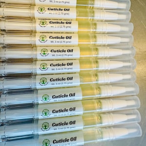 May include: A collection of cuticle oil pens, each with a clear tube and white applicator tip. The labels read "Cuticle Oil" and list ingredients. Each pen contains 3 ml of oil, approximately 0.10 fl oz.