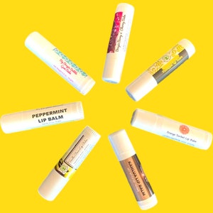 May include: An arrangement of lip balms on a yellow background. The lip balms are in white tubes with various labels, including "Big Bougie Bubble," "Peppermint Lip Balm," and "Kahlua Lip Balm." The text "Big Bougie Lip Balms!" is at the top.