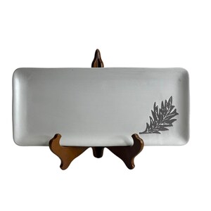 May include: White rectangular serving platter with a gray leaf design. The platter is on a wooden stand.