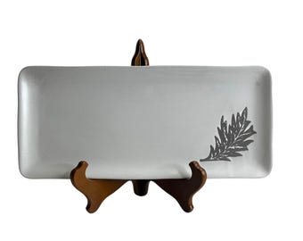 May include: White rectangular serving platter with a gray leaf design. The platter is on a wooden stand.