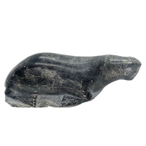 May include: A black stone sculpture of a seal lying down. The sculpture is carved in a realistic style and has a smooth, polished finish.