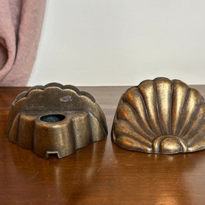May include: Two antique gold-toned metal decorative pieces shaped like seashells. The pieces have a scalloped edge and a raised design.