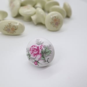 May include: A white ceramic cabinet knob with a pink rose and green leaves design.