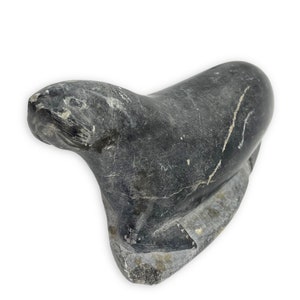 May include: A black marble sculpture of a seal lying on its belly. The sculpture is carved in a realistic style and has a smooth, polished finish.