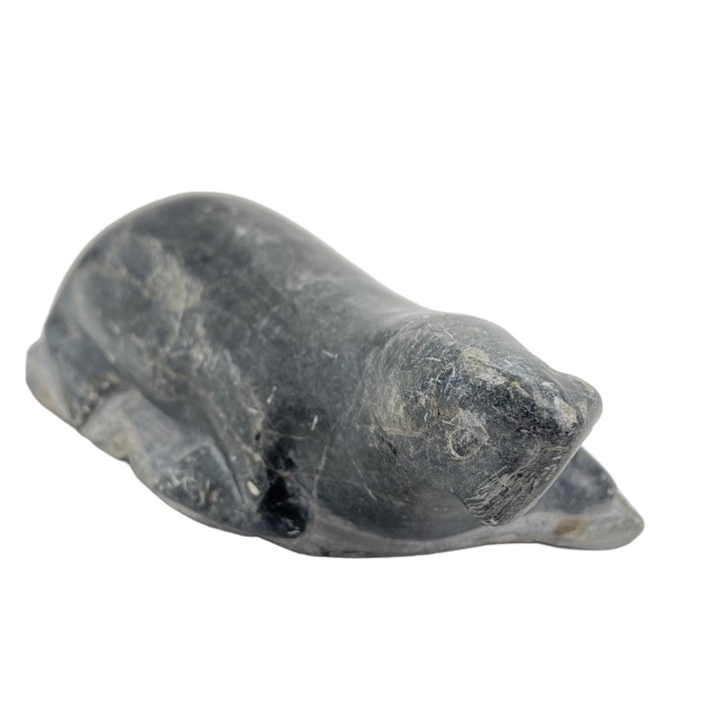 May include: A hand-carved stone sculpture of a seal, lying on its belly with its head turned to the side. The sculpture is made of dark gray stone with a smooth, polished finish.
