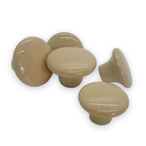 May include: Four beige ceramic cabinet knobs with a smooth, glossy finish. The knobs are round and have a slight mushroom shape.
