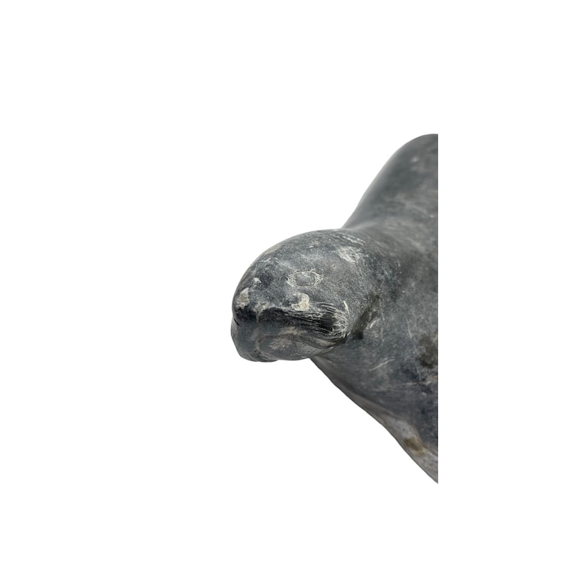 May include: A carved stone sculpture of a seal, with a gray and white color scheme. The seal is lying on its side, with its head turned to the side. The sculpture is made of a smooth, polished stone.