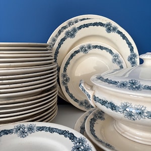 Peut inclure: Ensemble de vaisselle ancienne en céramique blanche avec un motif floral bleu. L'ensemble comprend des assiettes, des bols et un plat de service couvert. Les assiettes sont empilées et le plat de service a des poignées et un couvercle.