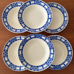 May include: A set of six round ceramic bowls, each featuring a white center and a wide rim decorated with a blue and white checkered grid pattern. The bowls are arranged in two rows of three, displaying a consistent design across all pieces.