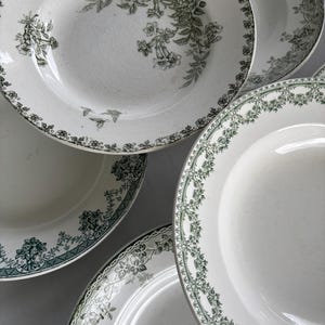 May include: A collection of white ceramic plates with green floral patterns. The plates feature intricate designs around the rims and in the center, showcasing a vintage aesthetic. The plates vary in size and shape, offering a classic tableware set.