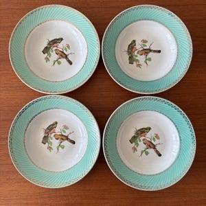 Pode incluir: Um conjunto de quatro tigelas de sopa redondas em cerâmica com centro branco e uma ilustração detalhada de dois pássaros num ramo. A borda larga é verde menta com textura canelada diagonal e um delicado acabamento dourado festonado.