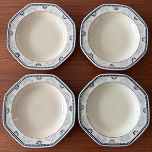 May include: Four octagonal cream-coloured bowls with a blue floral and dotted border. The bowls have a shallow depth and are arranged in a square formation on a wooden surface. The floral design is repeated around the rim of each bowl.