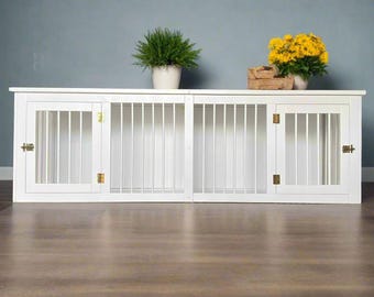 May include: White wooden double dog crate with two doors and brass hinges. The crate is sitting on a wooden floor.