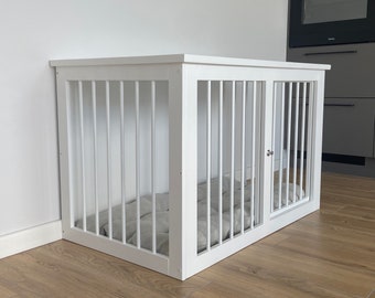May include: White wooden dog crate with a door and a white cushion inside. The crate is sitting on a light wood floor.