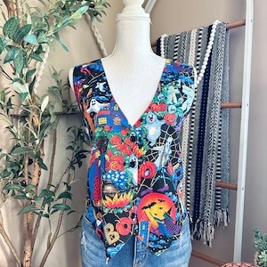 May include: A sleeveless vest featuring a vibrant Halloween-themed print on a black background, including ghosts, pumpkins, a witch on a broomstick, and a cauldron. The vest has a V-neckline and is fastened with four black buttons down the front.