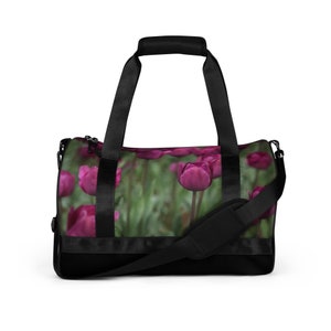 May include: Black duffel bag with a zipper closure and adjustable shoulder strap. The bag features a floral print of pink tulips on a green background.