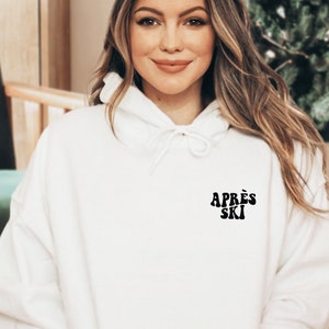 Könnte beinhalten: Weißer Kapuzenpullover mit dem Text "APRÈS SKI" in schwarzer Retro-Schrift.