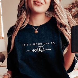 Könnte beinhalten: Dunkelblaues T-Shirt mit weißem Schriftzug "IT'S A GOOD DAY TO write". Das T-Shirt hat einen Rundhalsausschnitt und ist aus weichem Stoff. Ein tolles Geschenk für Schriftsteller und Schreibbegeisterte.