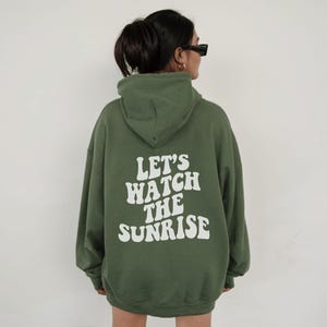 May include: A green hooded sweatshirt with the text "Let's watch the sunrise" printed in white on the back.