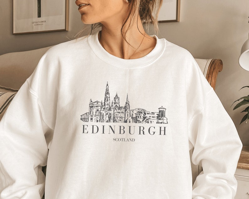May include: White sweatshirt with a black and white graphic of the Edinburgh skyline. The text "EDINBURGH SCOTLAND" is printed below the graphic.