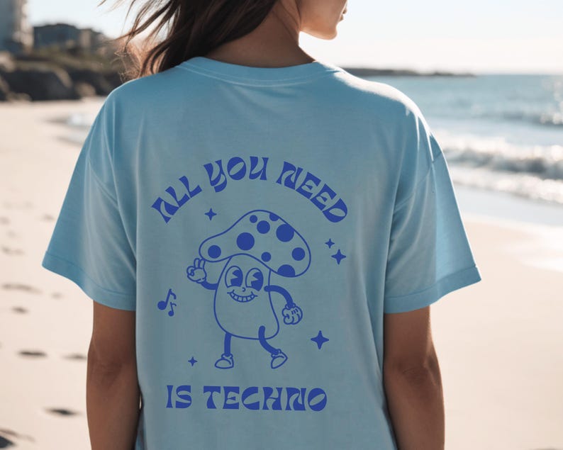 Puede incluir: Camiseta azul claro con un dise&ntilde;o retro en la espalda. El dise&ntilde;o presenta un personaje de dibujos animados de un hongo con el texto "ALL YOU NEED IS TECHNO" en azul. La camiseta es de corte holgado.