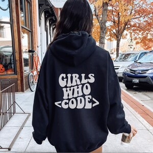 Könnte beinhalten: Schwarzer Kapuzenpullover mit dem Text "Girls Who <CODE>" in Weiß auf der Rückseite.