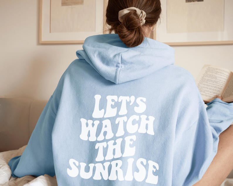 May include: A light blue hoodie with the text "Let's Watch The Sunrise" in white retro-style lettering.