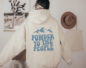 Könnte beinhalten: Cremefarbener Kapuzenpullover mit blauem Bergmotiv und dem Text "POWDER TO THE PEOPLE". Der Hoodie hat eine Kapuze mit Kordelzug und eine Kängurutasche. Das Design befindet sich auf der Rückseite des Hoodies.