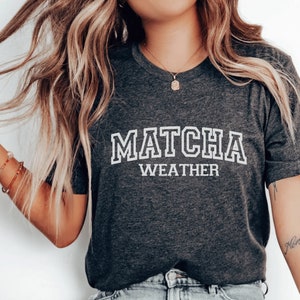 May include: A dark gray t-shirt with white text that reads "MATCHA WEATHER".