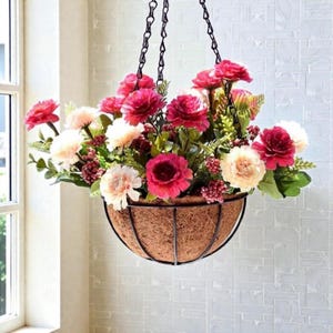 May include: Hanging flower basket filled with vibrant pink and cream-colored flowers. The basket is made of a woven brown material and is suspended by a black chain. The flowers are lush and full, creating a beautiful display.