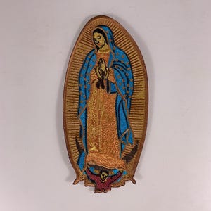 May include: Embroidered patch featuring the Virgin of Guadalupe. The patch has a gold border and background, with a blue cloak and orange dress. The image includes a detailed depiction of the Virgin Mary with clasped hands and a halo. The bottom of the patch has a red and black design.
