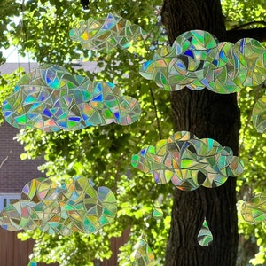 May include: A colourful mobile made of iridescent CDs shaped like clouds and raindrops hanging from a tree branch.