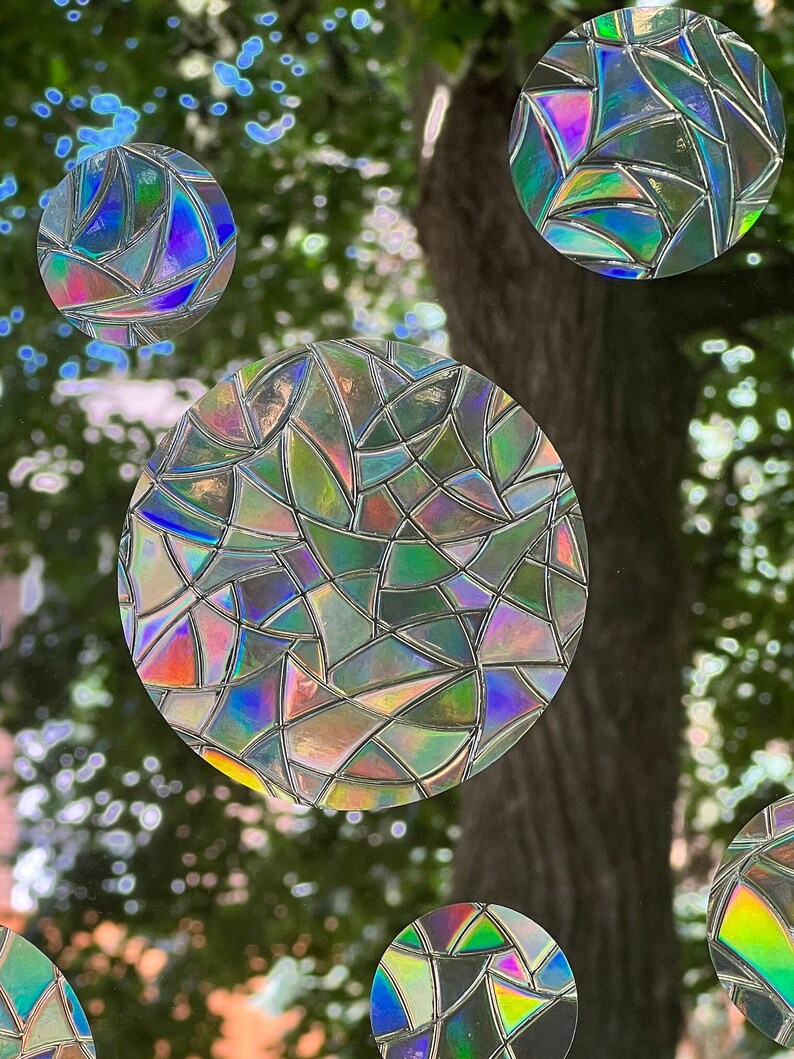 May include: A close-up of a window with several iridescent, circular stickers. The stickers are made of a mosaic of small, geometric shapes. The stickers are arranged in a random pattern on the window.