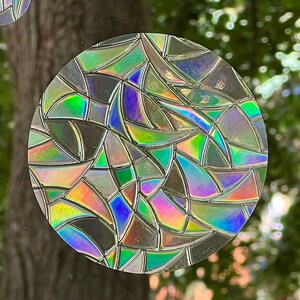 May include: A round, iridescent sticker with a geometric pattern of overlapping, curved shapes in shades of green, blue, purple, and pink.