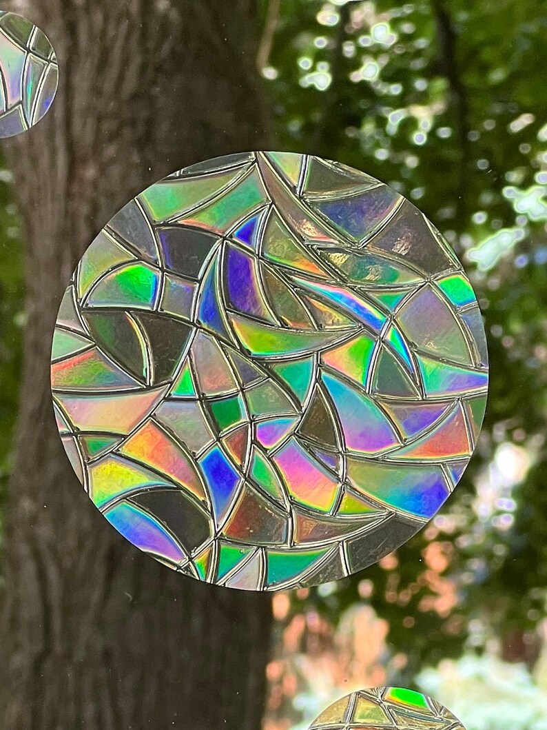 May include: A round, iridescent sticker with a geometric pattern of overlapping, curved shapes in shades of green, blue, purple, and pink.