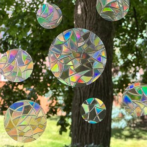 May include: A window with a view of a tree and green grass. The window is decorated with iridescent, circular stickers that resemble stained glass.