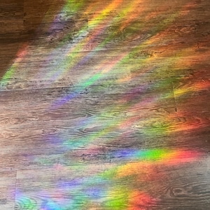 May include: A rainbow prism light shines on a wooden floor, creating colourful streaks of light.