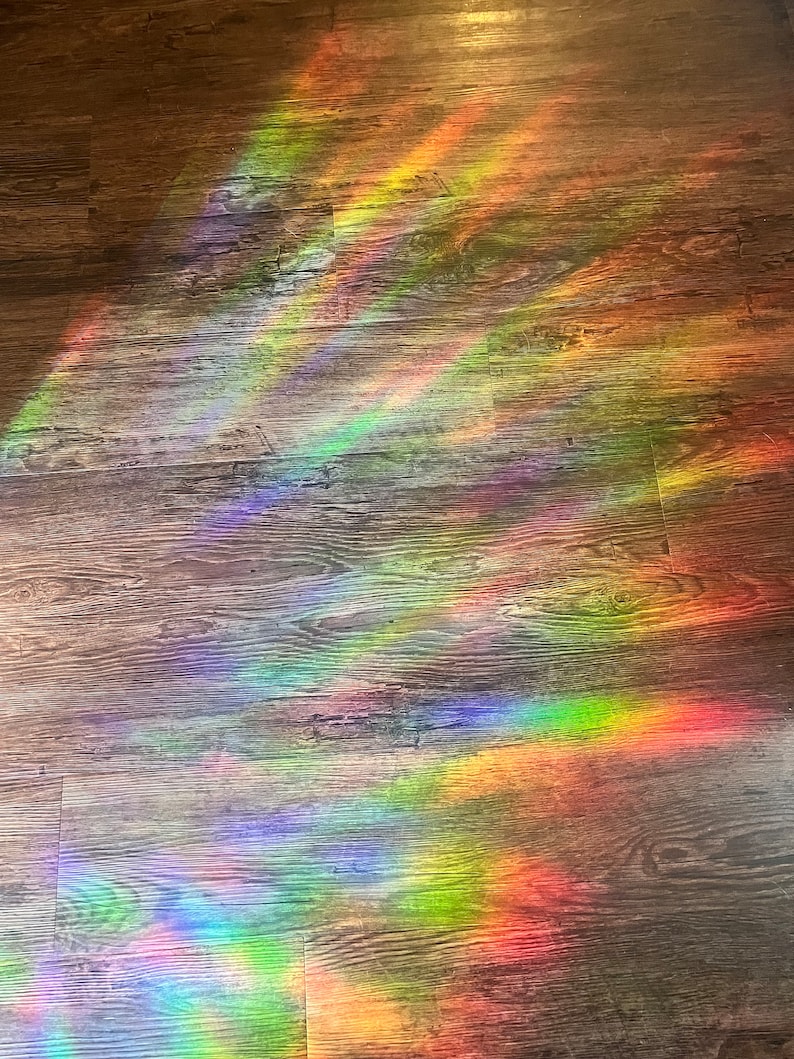 May include: A rainbow prism light shines on a wooden floor, creating colourful streaks of light.
