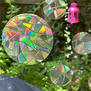May include: A close-up of a window with iridescent, circular stickers. The stickers have a stained glass pattern and are arranged in a random pattern on the window.