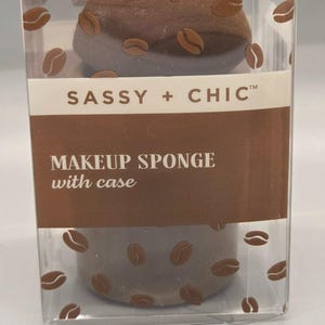May include: A brown makeup sponge with coffee bean designs, packaged in a clear plastic case. The case features the text "SASSY + CHIC" and "MAKEUP SPONGE with case". The sponge is a solid brown color.