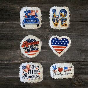 May include: Six fabric patches with patriotic themes. The patches are white with red, white, and blue designs. The designs include a truck with an American flag, the word "LOVE" with sunflowers, a heart with an American flag, the words "America Vibes", the words "God Bless America", and a peace sign, a heart, and the words "Peace Love America".