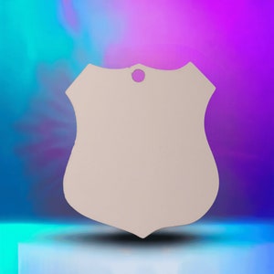 May include: A blank white shield-shaped ornament with a hole at the top for hanging. The ornament is made of a smooth, lightweight material and has a slightly rounded edge.