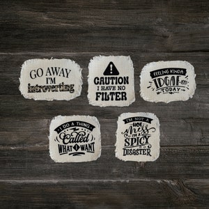 May include: Six white fabric patches with black text. The patches have sayings such as "Go Away I'm Introverting", "Caution I Have No Filter", "Feeling Kinda IDGAF-ish Today", "I Do A Thing Called What I Want", and "I'm Not A Hot Mess I'm A Spicy Disaster".
