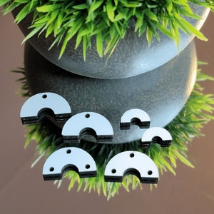 May include: Six silver-colored metal half-circle shapes with a hole at the top. The shapes are stacked on top of each other and are arranged in a semi-circle.