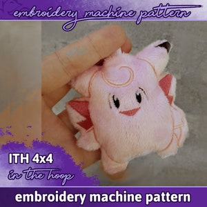 Könnte beinhalten: Rosa Plüschtier mit gestickten Details, das einem Comic-Charakter ähnelt. Das Spielzeug wird in einer Hand gehalten. Der Text "ITH 4x4 in the hoop" ist in der linken unteren Ecke des Bildes sichtbar. Der Text "embroidery machine pattern" ist oben und unten im Bild sichtbar.
