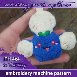 Può includere: Un giocattolo di peluche blu con una testa bianca e soffice e due braccia bianche. Il giocattolo ha un viso sorridente con guance rosse e una lingua rosa che sporge. Il giocattolo è etichettato con "ITH 4x4 in the hoop" e "embroidery machine pattern".