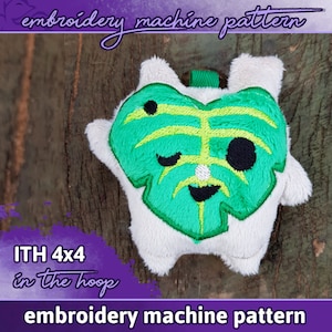 May include: A plush toy with a green leaf design and a smiling face, embroidered on a white body. The text "embroidery machine pattern" and "ITH 4x4 in the hoop" are visible. The toy is approximately 4 inches by 4 inches.