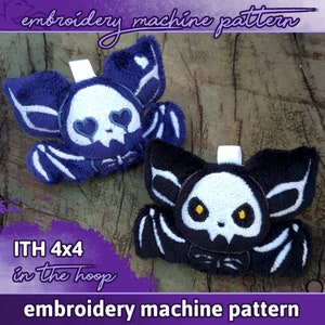 May include: Two plush bat toys with embroidered skull faces. The bat on the left is blue with white eyes and a heart-shaped pupil. The bat on the right is black with yellow eyes. Both bats have white wings and are labeled "ITH 4x4 in the hoop" and "embroidery machine pattern".