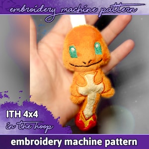 May include: Embroidered plush toy of a small orange and yellow creature with green eyes. The toy is held in a hand and is labeled "ITH 4x4 in the hoop embroidery machine pattern".