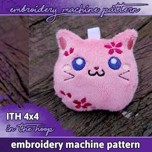 Może przedstawiać: Różowy pluszowy kot z haftowanymi detalami, w tym oczami, wąsami i uśmiechającym się pyskiem. Kot ma haftowane różowe kwiaty na swoim ciele. Obraz zawiera tekst "ITH 4x4 in the hoop" i "embroidery machine pattern".